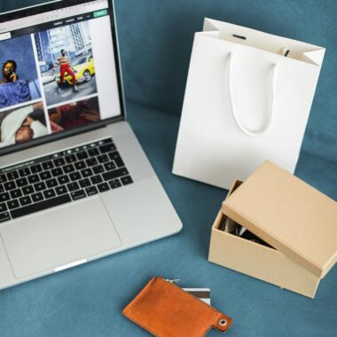 A high-angle view of online shopping items including a laptop, gift bags, and wallet on a blue surface.