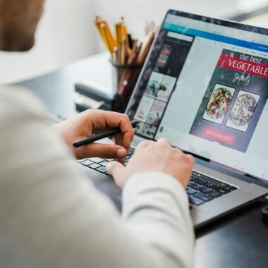 A man working on graphic design projects at a laptop in a well-lit office space.