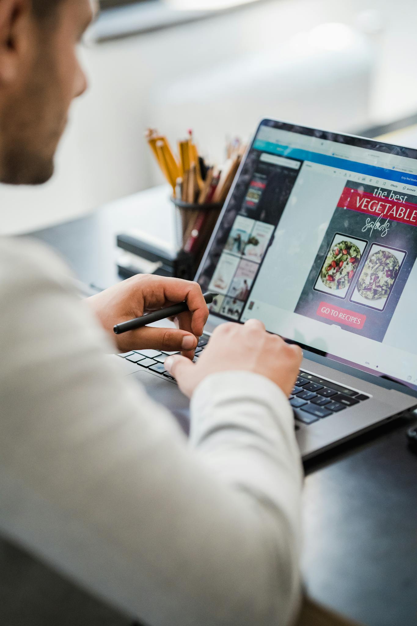 A man working on graphic design projects at a laptop in a well-lit office space.