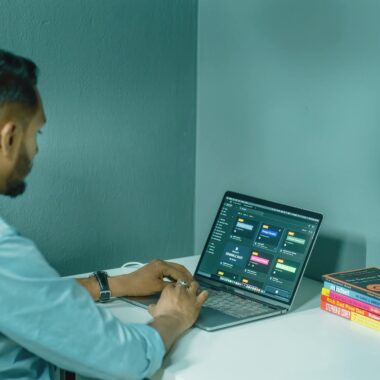 Focused man working on laptop at home office desk, surrounded by books and smartphone for a productive work environment.